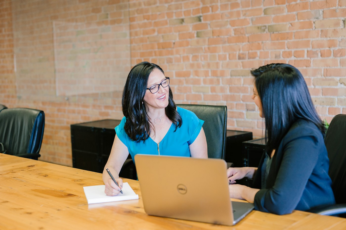 Two colleagues talking across a table with a notebook and a laptop