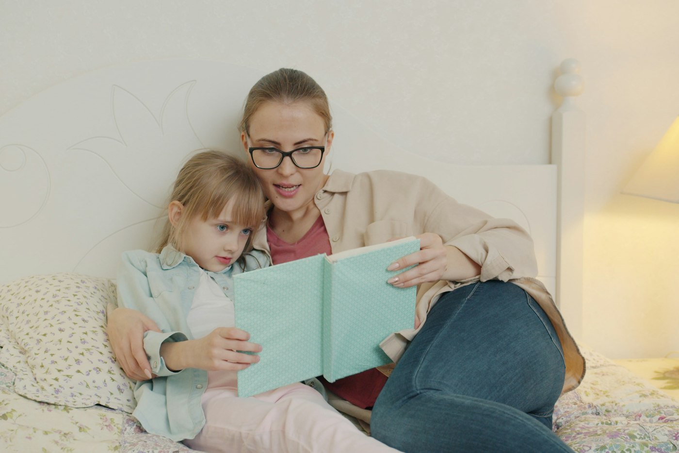 An adult reading a book with a young girl in bed