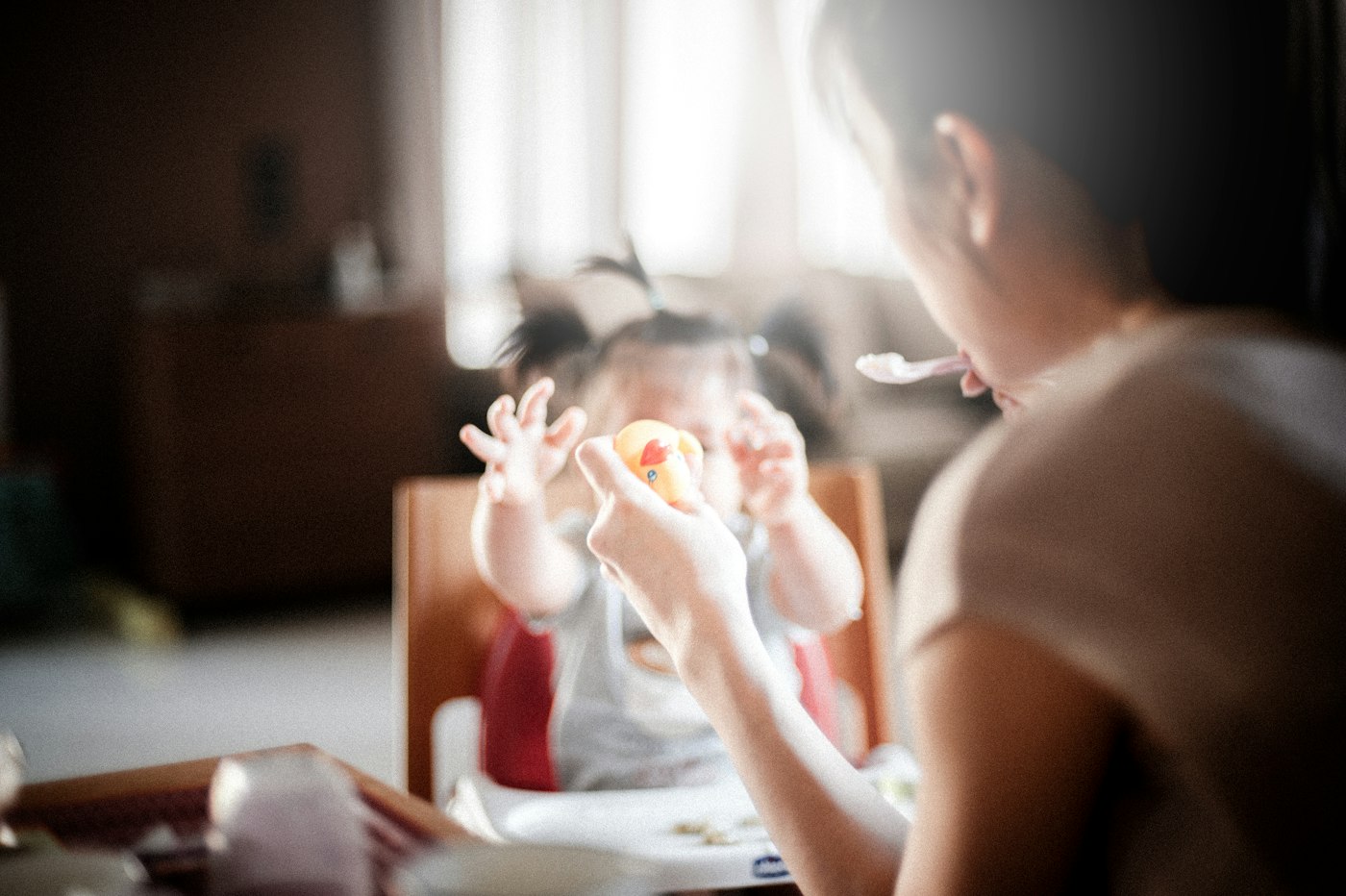 An adult sitting close to a young child in a high chair at mealtime