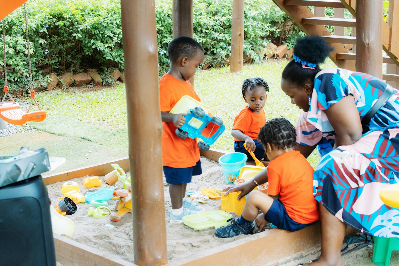 Children playing in an outdoor sandpit with a practitioner beside them