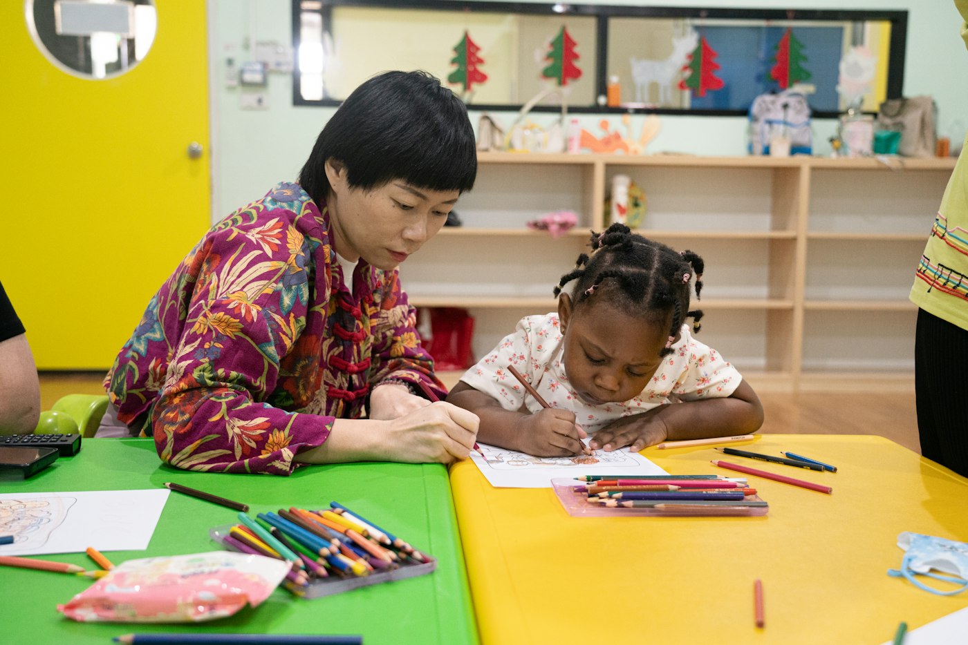 A practitioner and a young child drawing together at a nursery table