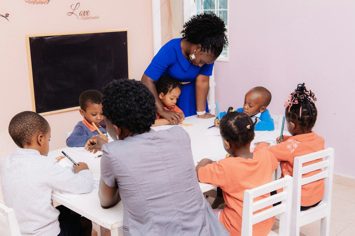 A practitioner guiding a small group of children drawing at a table