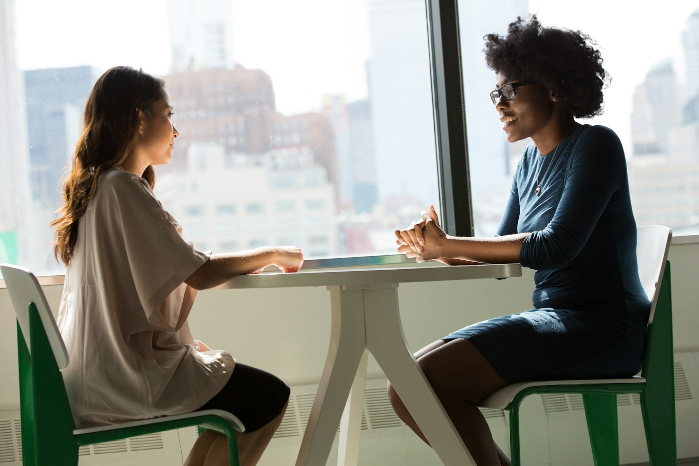 Two women talking across a small table by a window