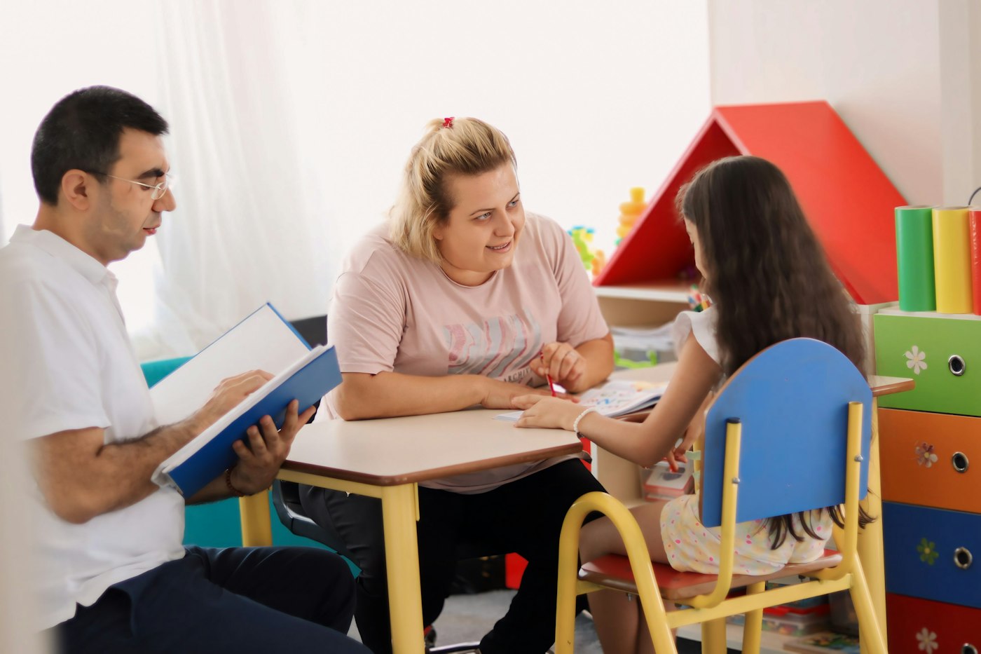 Adults and a child talking together around a table in an early years room